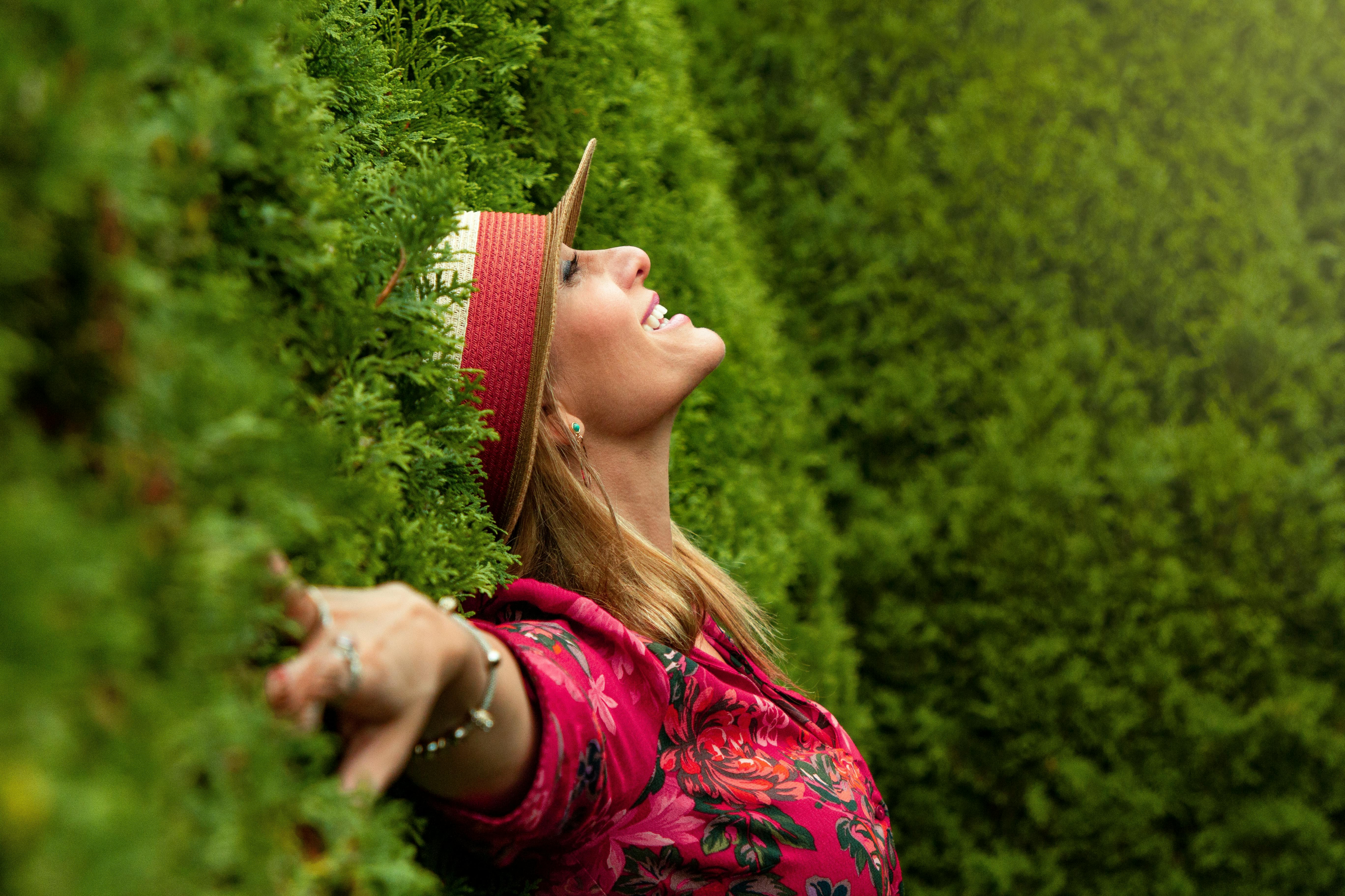 Femme souriante, bras en croix, dos contre un buisson – état de soulagement et de retour à soi – Emmanuelle Lecuyer accompagnement nutritionnel et énergétique 