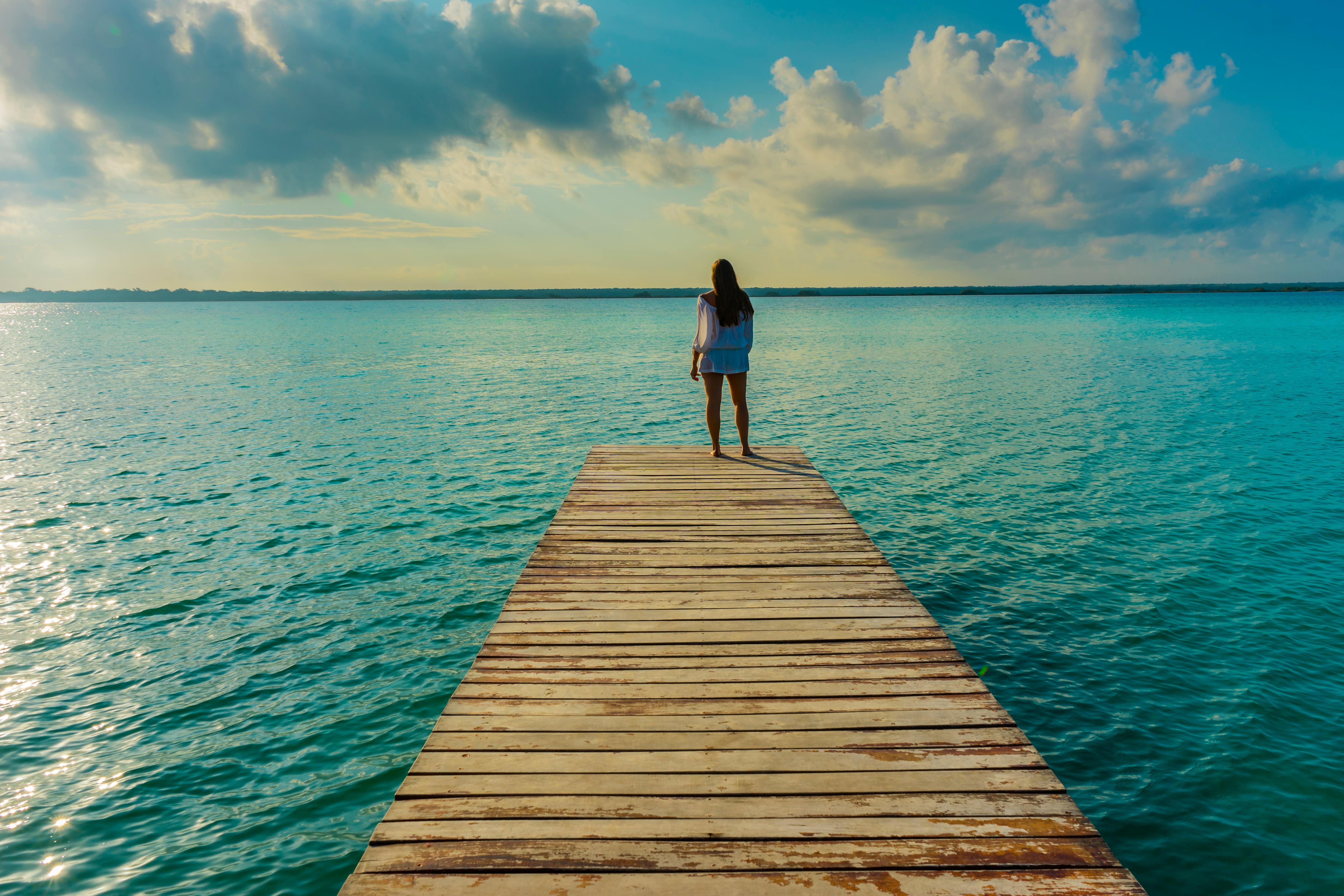 Femme regardant l’horizon depuis un ponton, mer bleue et ciel lumineux – symbole d’espoir, de clarté et de renouveau – accompagnement Emmanuelle Lecuyer